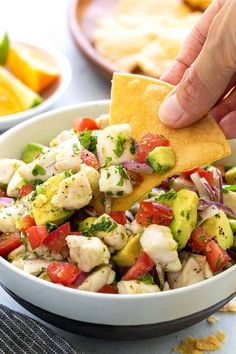 a hand holding a tortilla chip over a bowl filled with shrimp and veggies