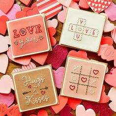 three decorated cookies sitting on top of a table covered in hearts and paper cut outs