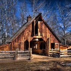 an old barn sits in the middle of a field with trees and fence around it