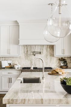 a kitchen with marble counter tops and white cabinets, an island style sink and two hanging lights