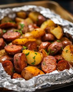 cooked potatoes and sausages in foil on a tray with parsley sprig