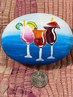 painted rocks with cocktails on them are next to a dime coin and pink towel