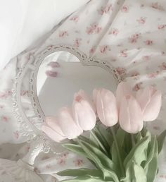 a bouquet of pink tulips in front of a heart shaped mirror on a bed