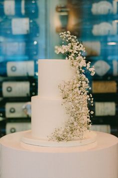 a three tiered cake with white flowers on top is displayed in front of a glass case