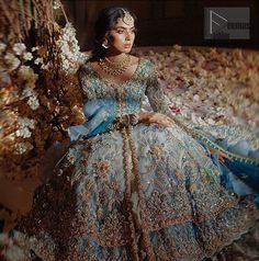 a woman in a blue and gold dress sitting on a couch with flowers behind her