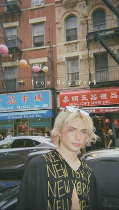 a woman with blonde hair and glasses standing in front of a building on a city street