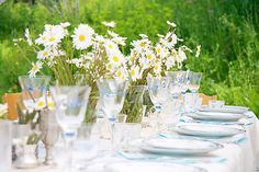 the table is set with white and blue plates, silverware, and daisies