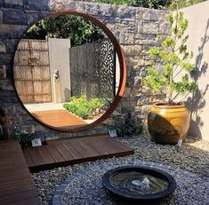 a circular mirror sitting on top of a stone wall next to a wooden table and potted plant