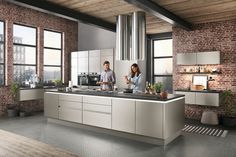 two people standing in a kitchen with brick walls and flooring, one woman is cooking while the other man is preparing food