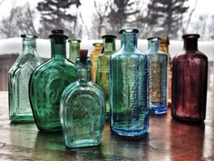 many different colored glass bottles lined up on a wooden table with trees in the background