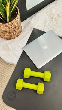 two yellow dumbs sitting on top of a yoga mat next to a laptop computer