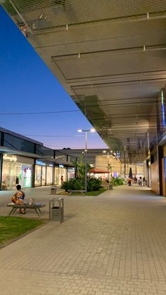 a person sitting on a bench in front of a shopping center at night with the lights on