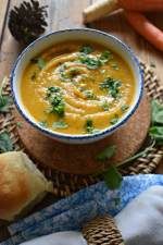 a bowl of soup with bread and carrots on the side