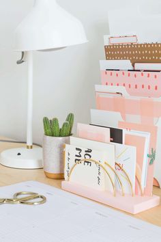 a desk topped with lots of office supplies next to a white lamp and a potted plant