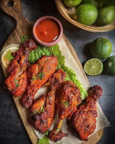 chicken wings with lettuce and sauce on a cutting board next to limes