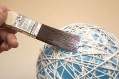 a person holding a paintbrush over a ball of string - wrapped material that is blue and white