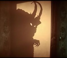 the shadow of a demon head is cast on a wall in a dimly lit room