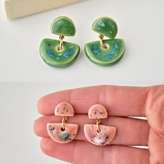 two pieces of jewelry sitting on top of a white table next to a person's hand