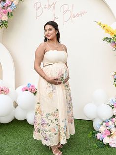 a pregnant woman standing in front of a backdrop with balloons and flowers on it's sides