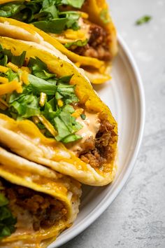 three tacos on a white plate topped with cheese and cilantro