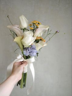 a person holding a bouquet of flowers in their left hand and wearing a white ribbon around it