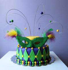 a mardi gras mask on top of a purple and green cake with beads