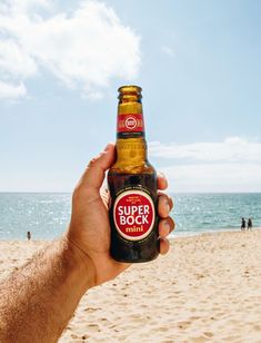 a person holding up a beer on the beach