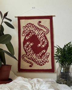 a red and white wall hanging next to a potted plant on top of a bed