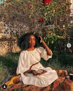 a woman is sitting on the ground with her hair blowing in the wind and holding a cell phone