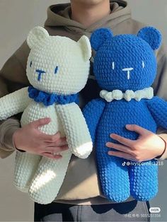 a man holding two teddy bears made out of knitted material, one is blue and the other is white