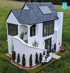 a doll house with a car parked in front of it on the grass next to a fence