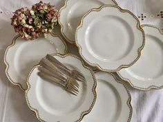 four white plates with gold trim and silver forks on them, next to a flower