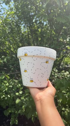 a hand holding up a cup with bees on it in front of some trees and bushes