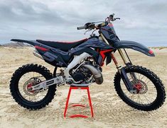 a dirt bike parked on top of a red stand in the sand at the beach