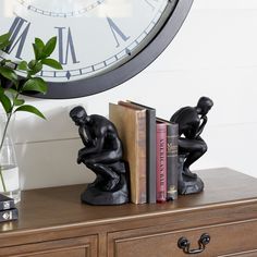 there is a clock on the wall behind two books and a vase with flowers in it