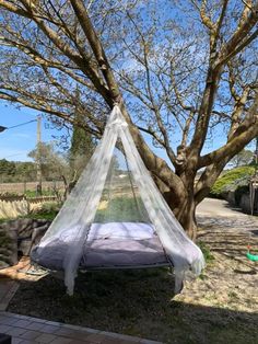 a bed with a mosquito net hanging from it's side in front of a tree