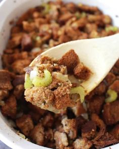 a white bowl filled with food and a wooden spoon holding up a piece of bread