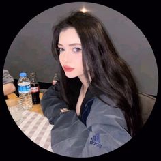 a woman with long black hair sitting at a table next to water bottles and a bottle of water