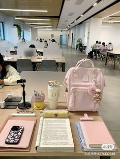 a pink backpack sitting on top of a wooden table next to a notebook and cell phone