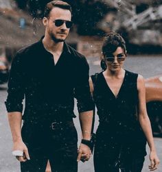 a man and woman walking down the street holding hands while wearing black outfits with sunglasses