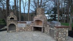 an outdoor stone pizza oven with grills on it's sides and trees in the background