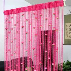 the pink curtain is hanging from the ceiling and has gold beads on it's sides