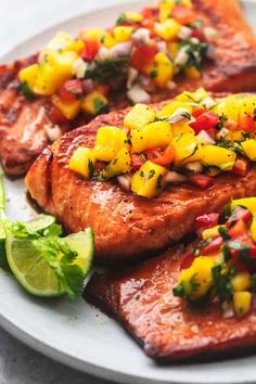 grilled salmon with pineapple salsa and lime wedges on a white platter