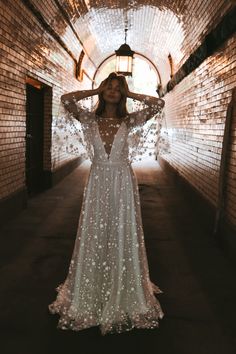 a woman in a long white dress standing in a tunnel with her arms behind her head