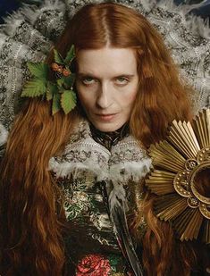 a woman with long red hair wearing a crown and holding a large gold sunflower