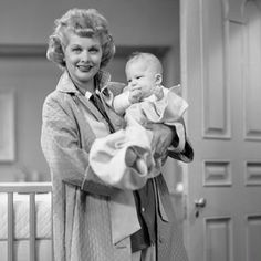 a woman holding a baby in her arms and standing next to a crib with doors