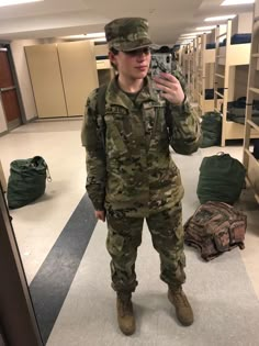 a woman in uniform taking a selfie with her cell phone while standing in a room full of bunk beds