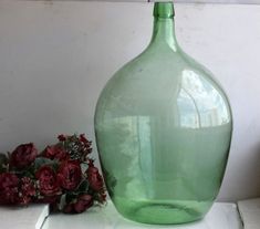 a large green vase sitting on top of a white table next to red flowers and greenery