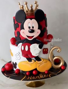 a mickey mouse cake is decorated with red and white frosting, gold trimmings, and a crown on top