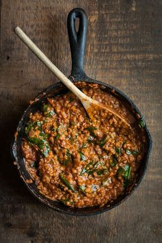 a skillet filled with red sauce and spinach on top of a wooden table